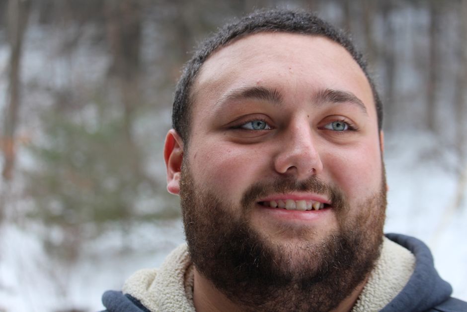 Close-up portrait of a smiling man with a beard and blue eyes in a snowy outdoor setting.
