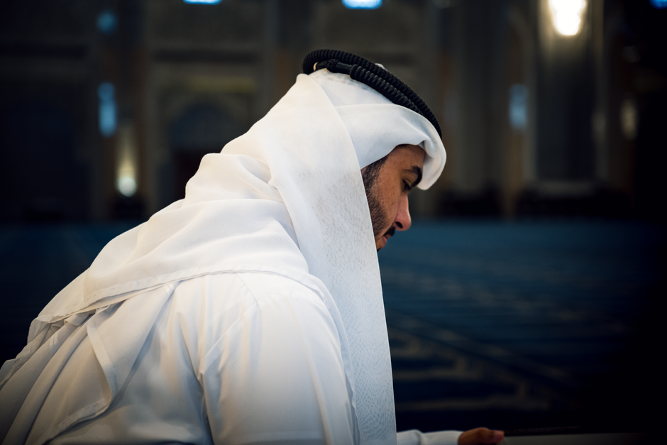 A man in traditional attire reflecting inside a mosque in Kuwait City, Kuwait.