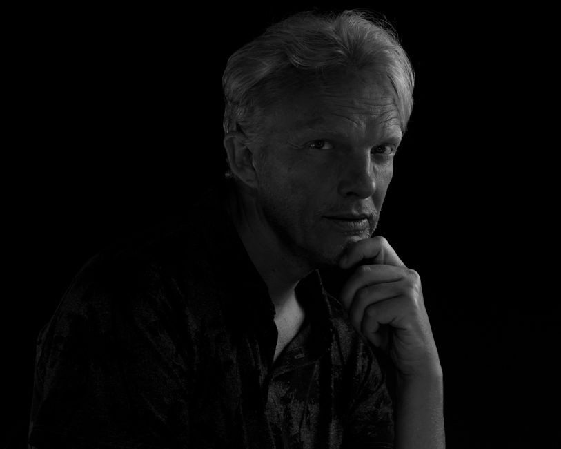 Dramatic black and white portrait of an elderly man in thoughtful pose against a dark background.