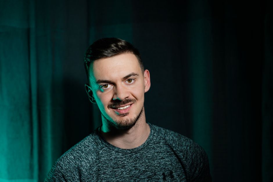 Portrait of a smiling adult male in a studio with a dark green background, exuding confidence and warmth.