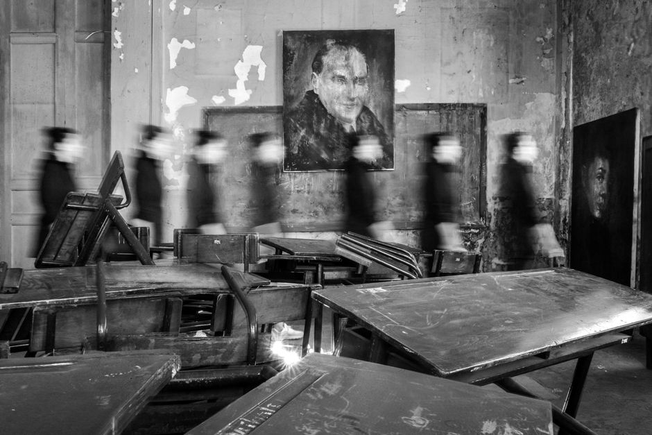Blurry figures move in a dilapidated room with striking portraits and overturned tables.