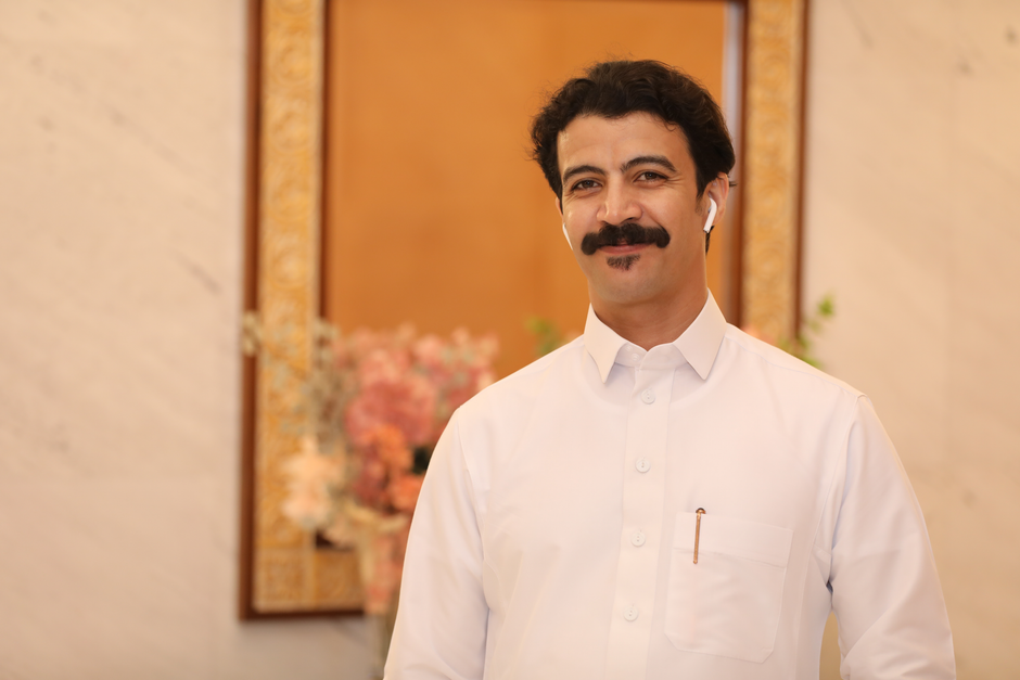 Portrait of a smiling man with a mustache wearing white in an indoor setting.